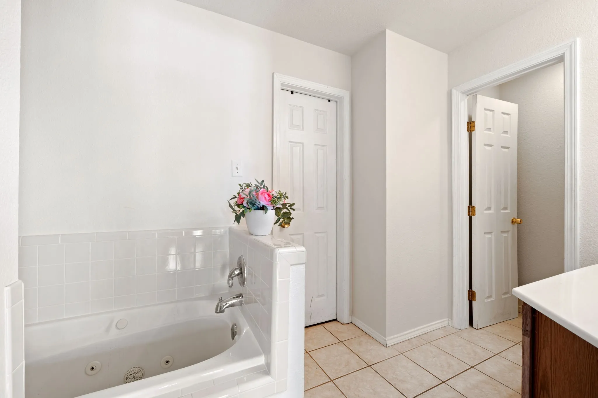 Primary Bathroom Jetted soaking tub with white tile surround, tile flooring, white walls, and two paneled doors
