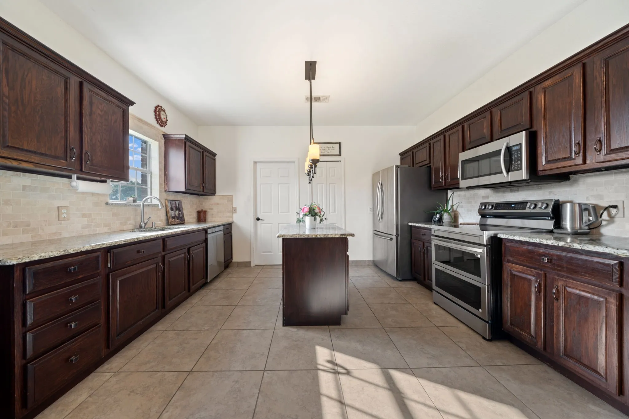 Kitchen featuring dark wood cabinetry, light granite countertops, a tiled backsplash, stainless steel appliances, and tile flooring