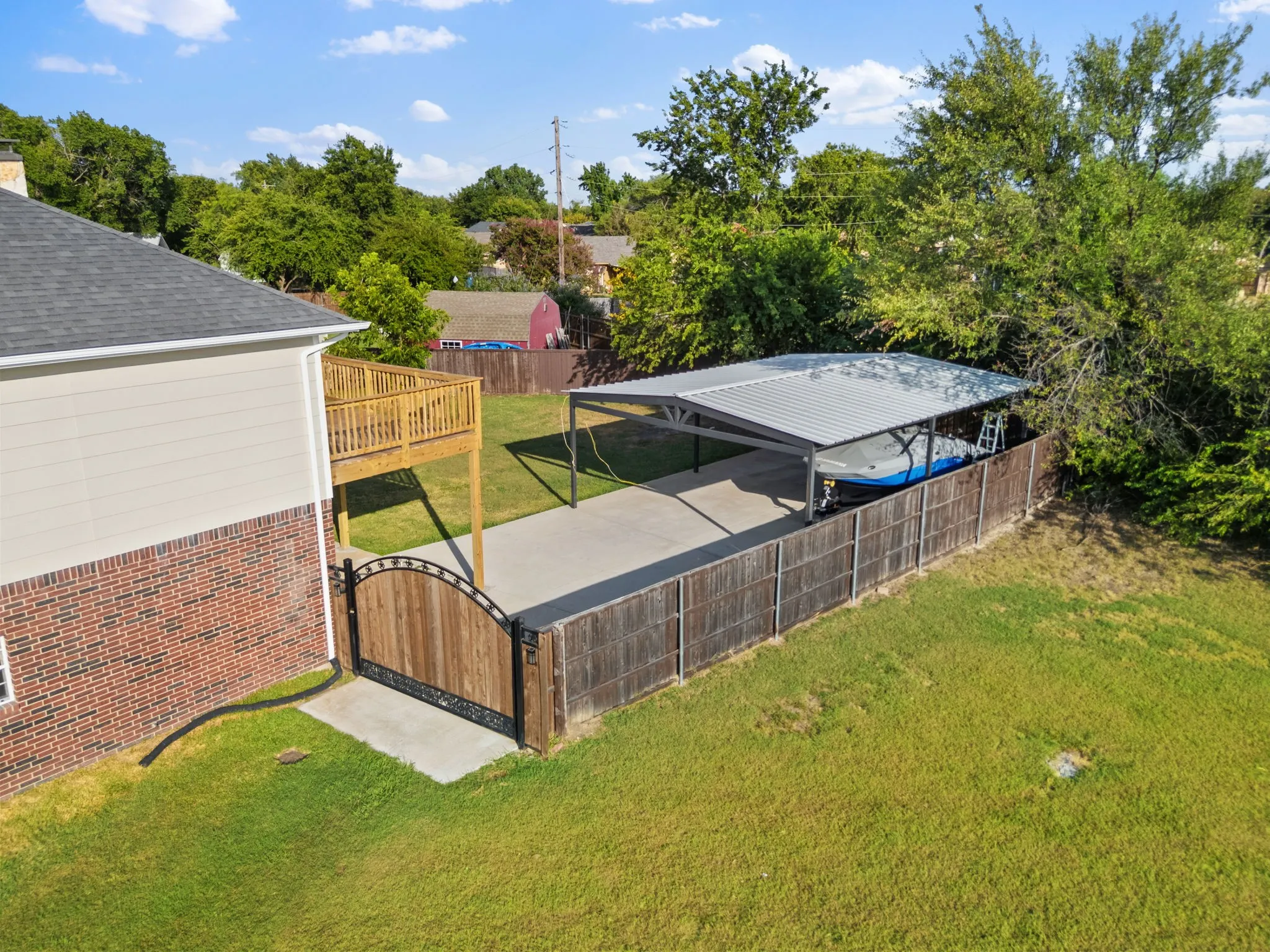 Property exterior featuring a carport with a metal roof, a wooden privacy fence, a wood deck with railings, and a side-entry wooden gate with wrought iron accents
