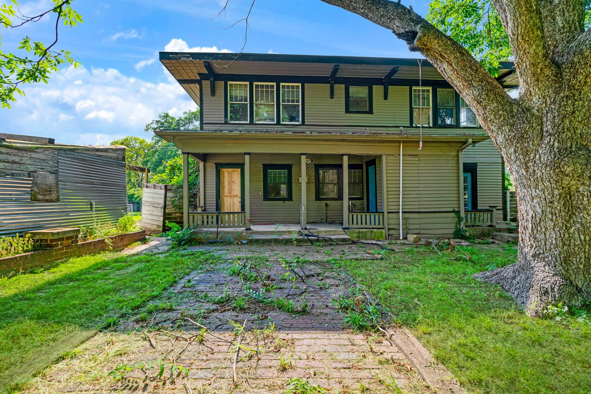 Two-story house featuring an expansive front porch, large mature tree, and a second-story dormer