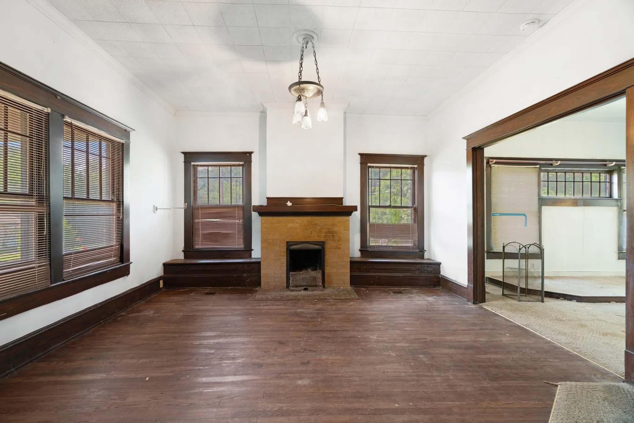 Spacious room featuring rich wood-finish flooring, a traditional fireplace with a brick surround, and multiple windows with dark wood trim