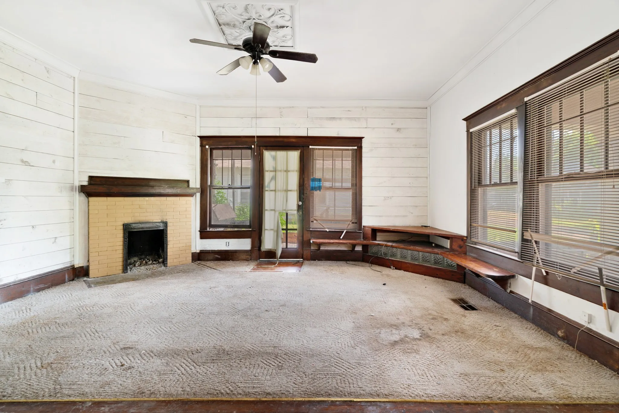Room featuring a neutral-toned brick fireplace with a dark wood mantel, white shiplap-style wall paneling, a ceiling fan, and dark wood trim around windows and doors
