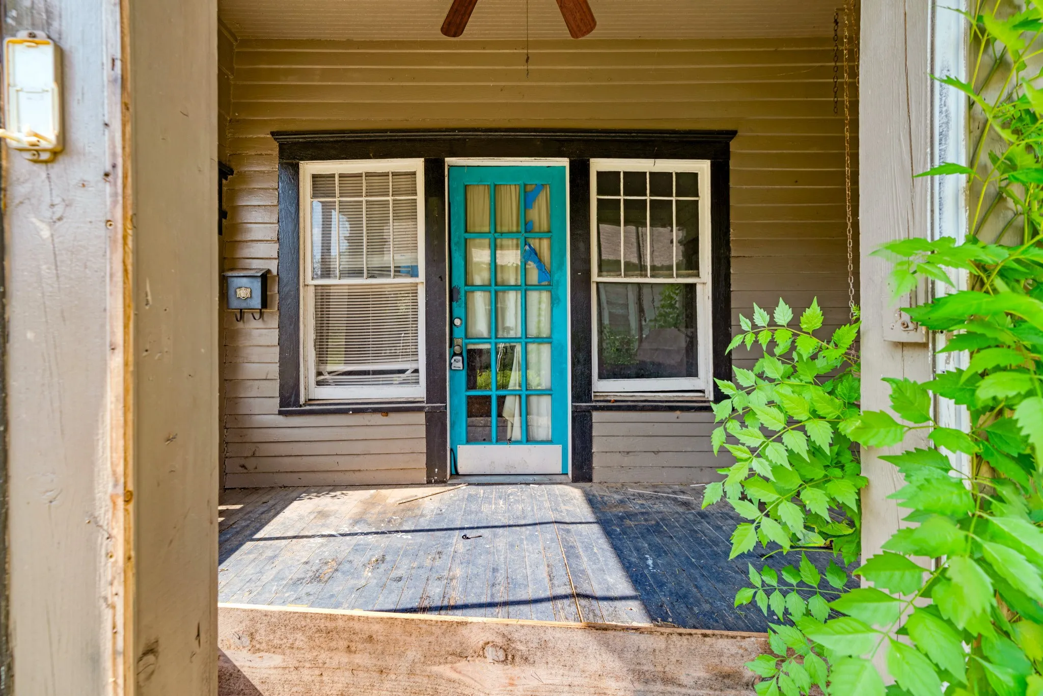 Side entry with covered porch with wood flooring, featuring a vibrant teal entry door with glass panels and sidelight windows