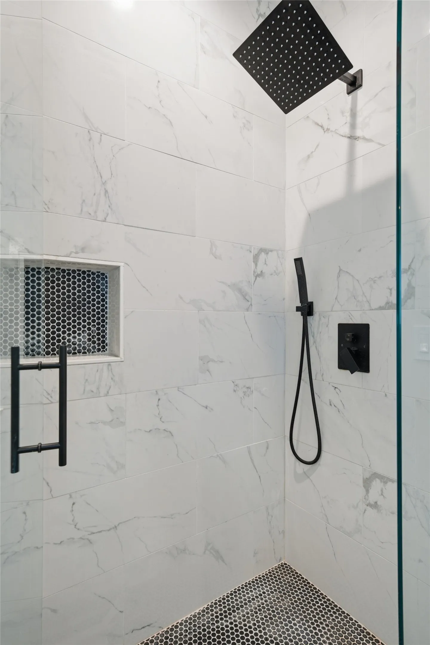 Walk-in shower with large format marbled wall tiles and black penny tile flooring