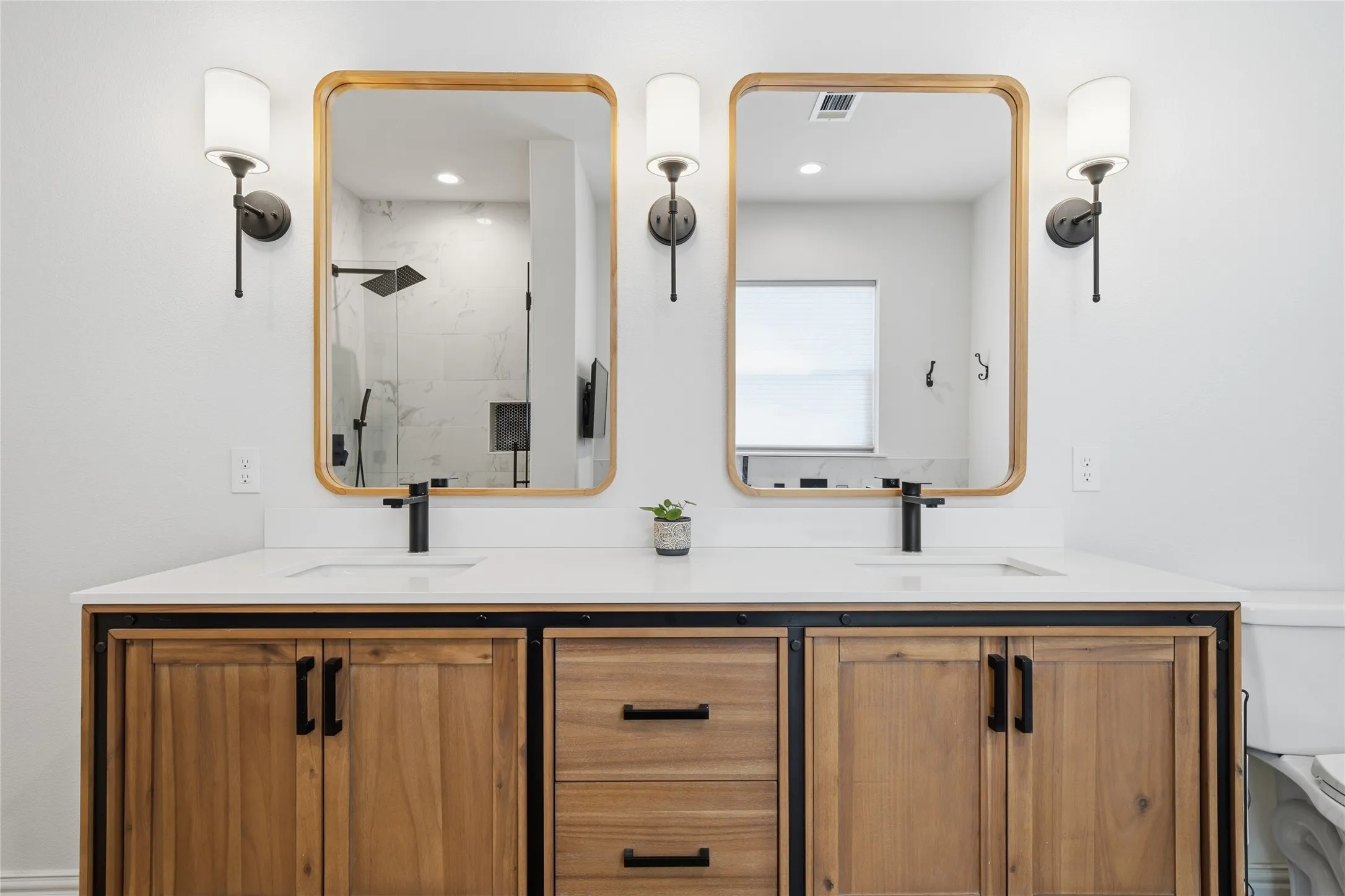 Dual vanity featuring wood-finish cabinetry, white countertops, rectangular undermount sinks, and matte black fixtures