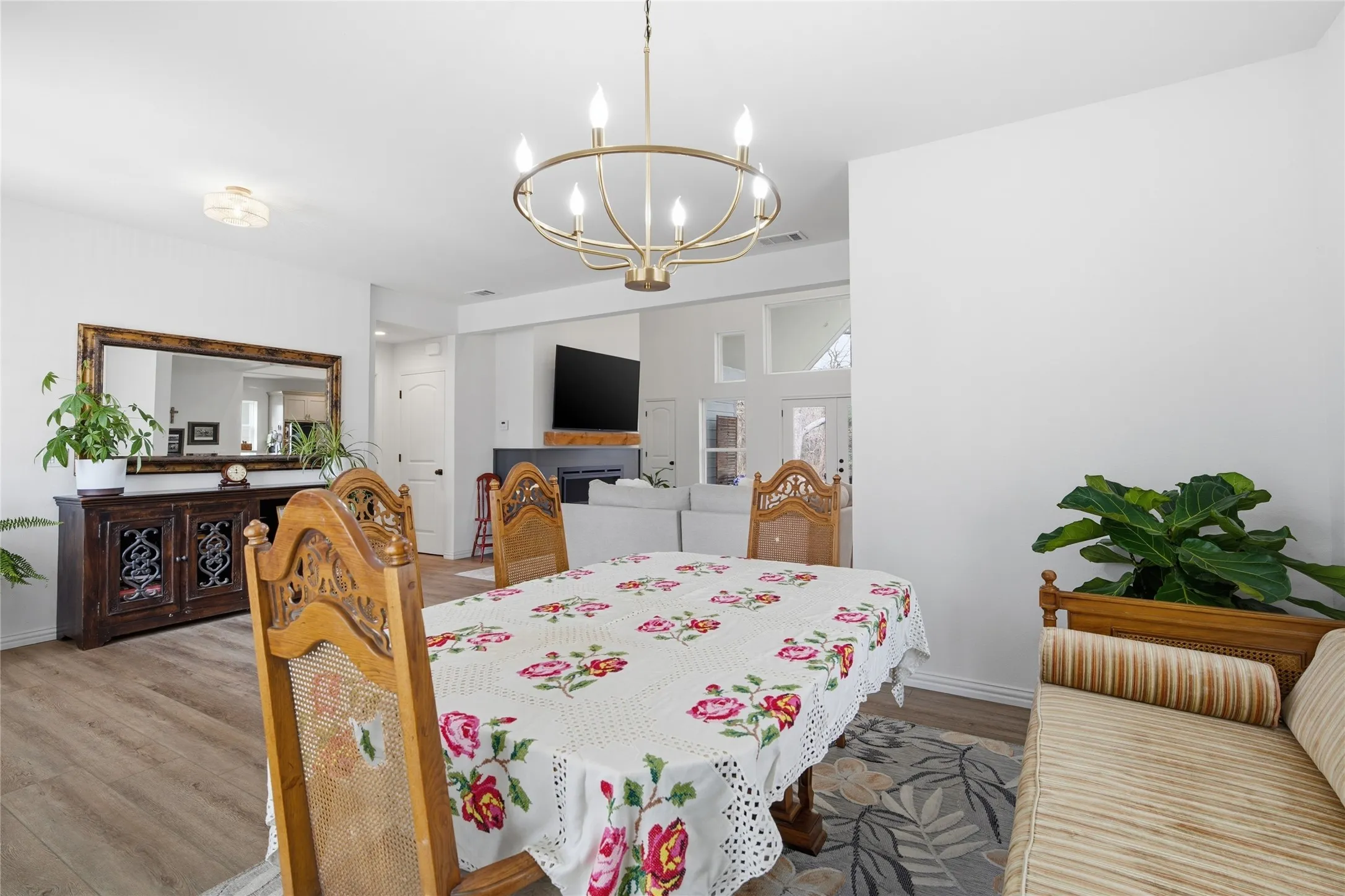 Dining area with wood-finish flooring, a contemporary chandelier, and an open layout connecting to an additional living space
