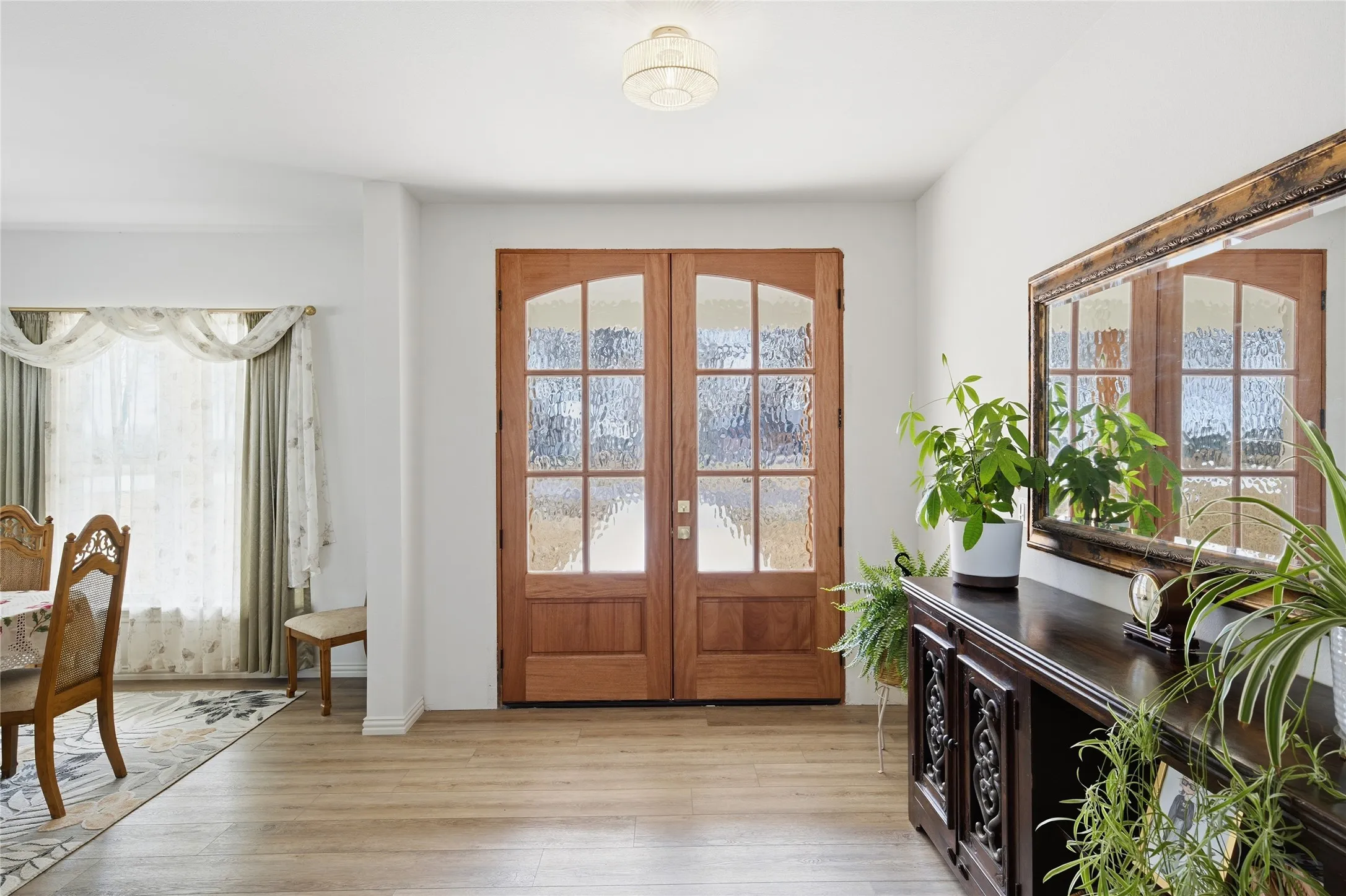 Double wooden entry doors with arched lites and textured glass, complemented by light wood-finish flooring