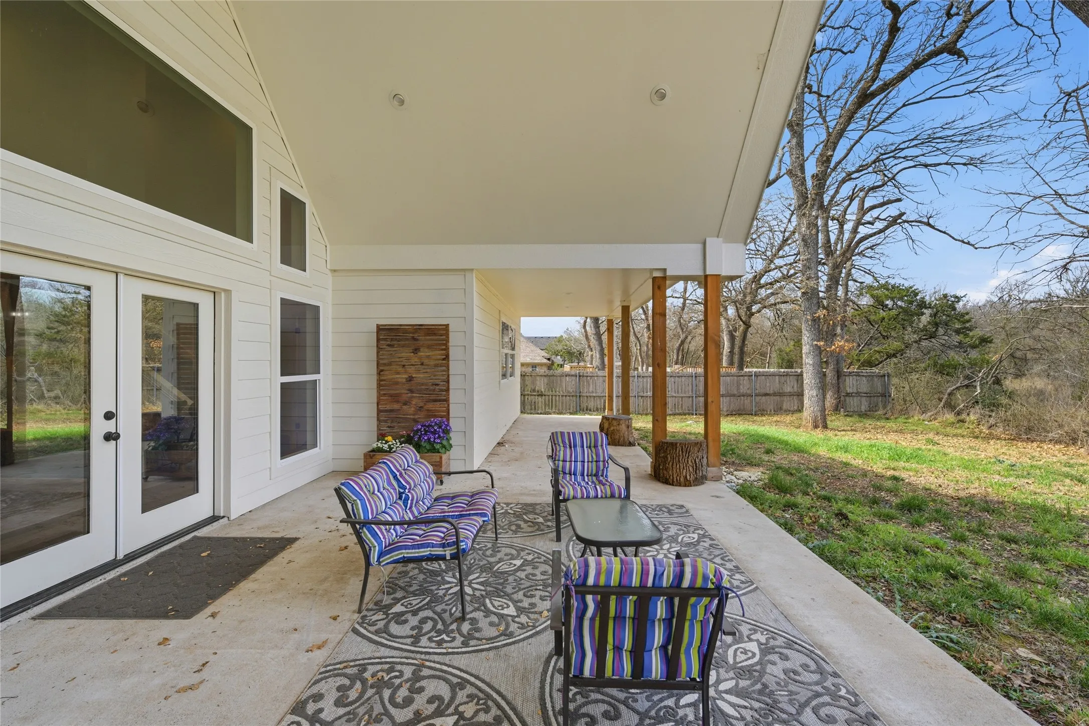 Expansive covered patio featuring a concrete surface, exposed wood support columns, and an exterior wall with white siding