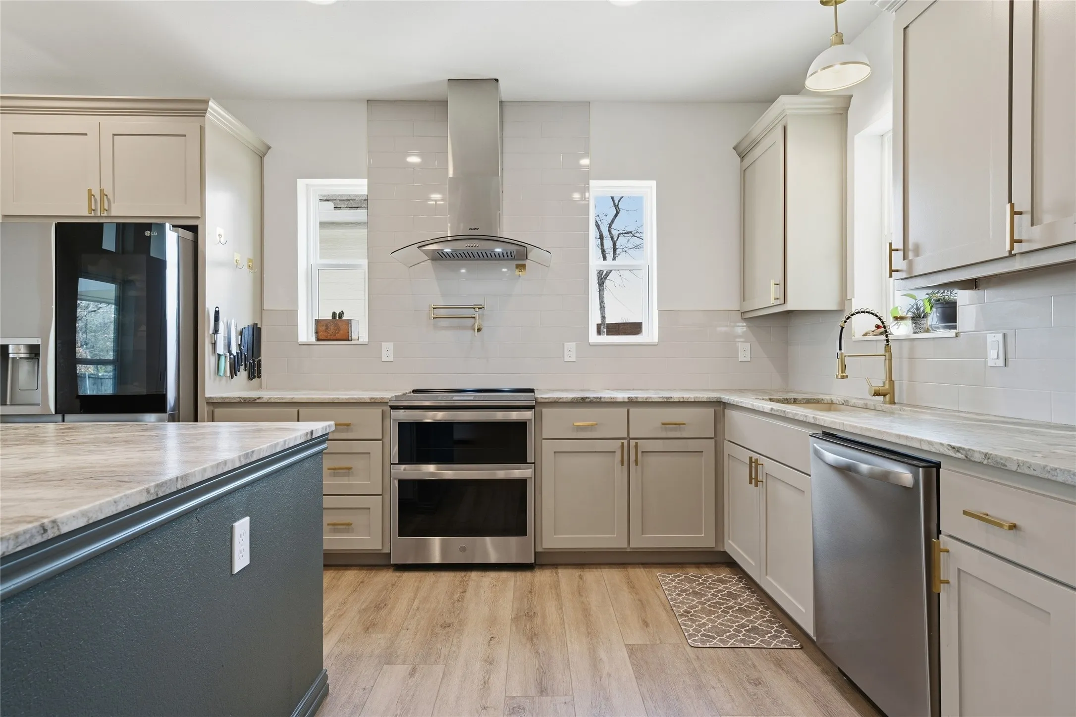 Modern kitchen featuring light wood-finish flooring, two-tone cabinetry, stainless steel appliances, and light-colored countertops