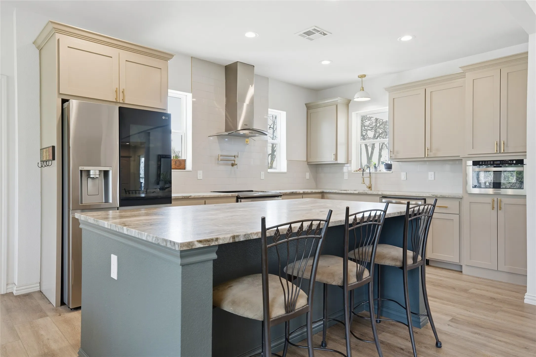 Kitchen featuring an oversized island with a stone countertop, light-toned cabinetry, stainless steel appliances, a tile backsplash, and wood-finish flooring
