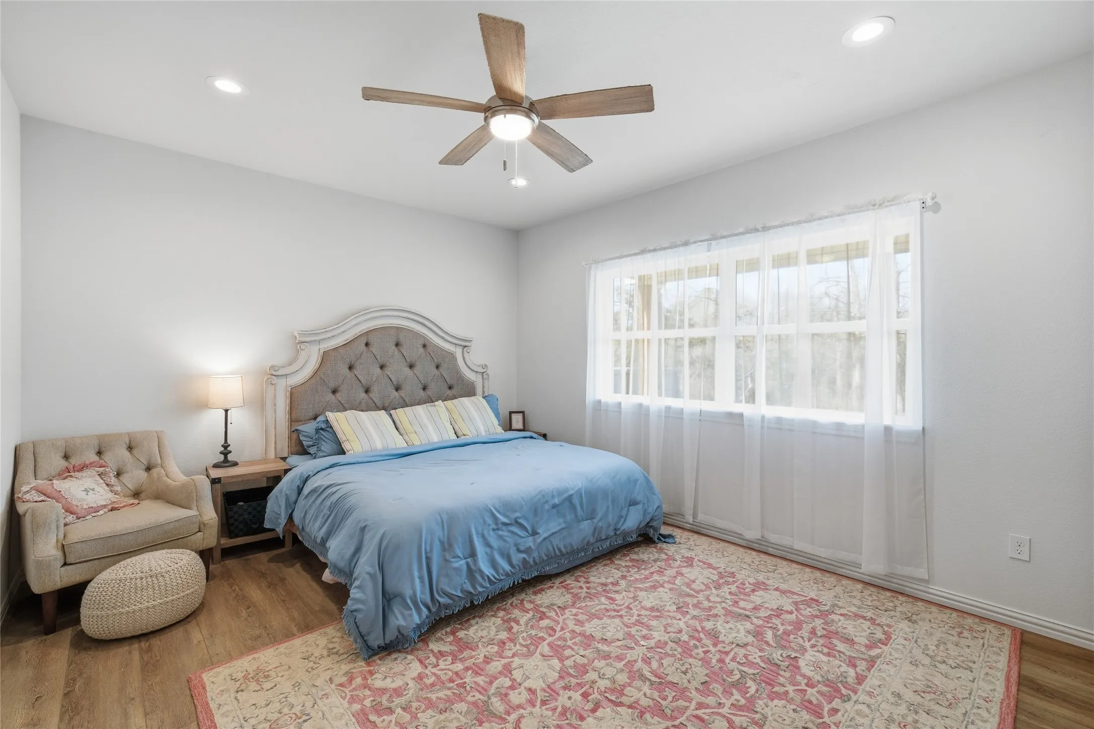 Spacious room featuring wood-finish flooring, a large multi-pane window, recessed lighting, and a ceiling fan with light fixture