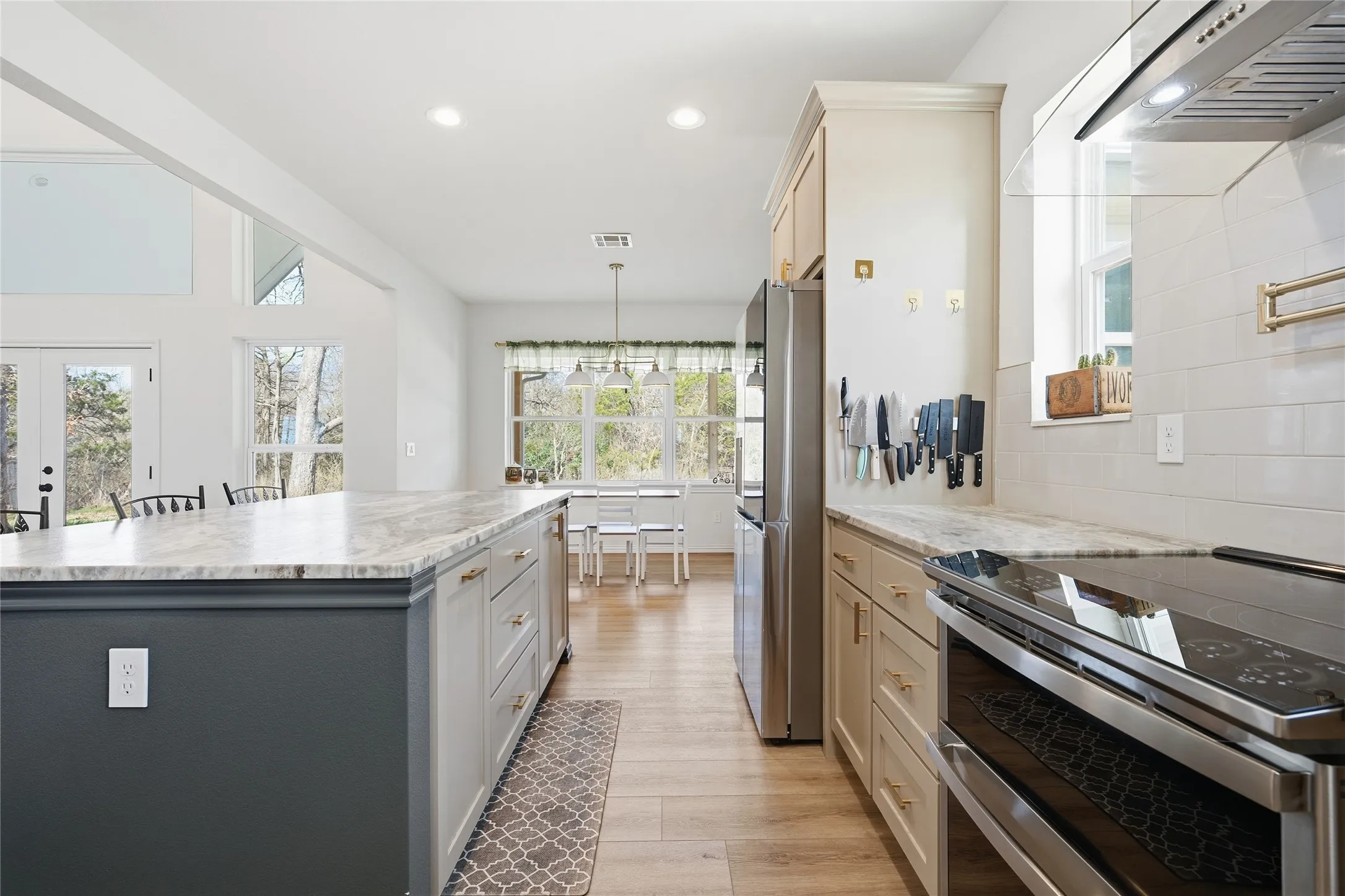 Galley-style kitchen featuring white cabinetry, stainless steel appliances including a built-in range and refrigerator, quartz countertops, subway tile backsplash, wood-finish flooring, and abundant natural light from multiple windows