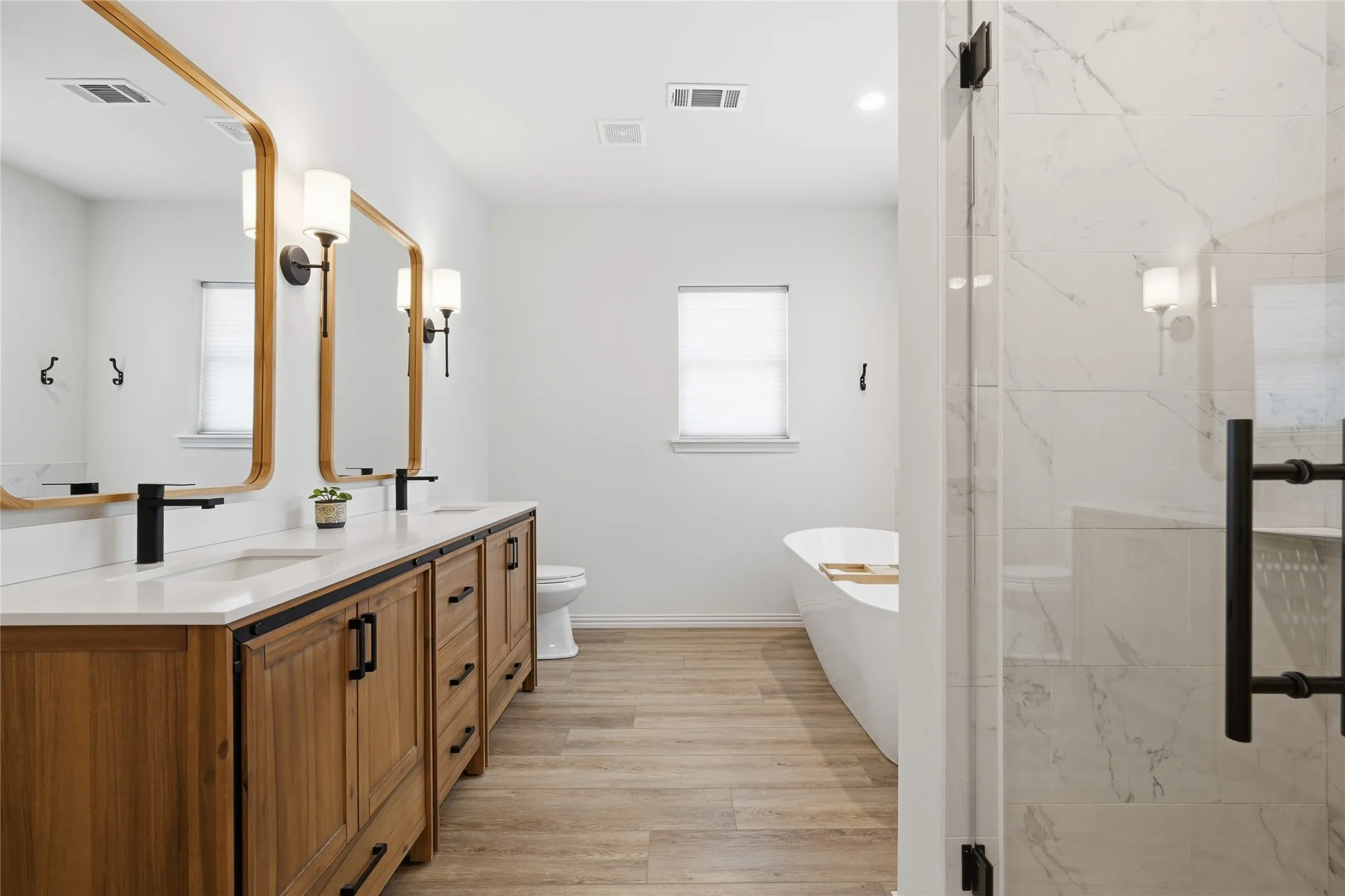Double vanity with wood-finish cabinetry, white countertops, and matte black fixtures