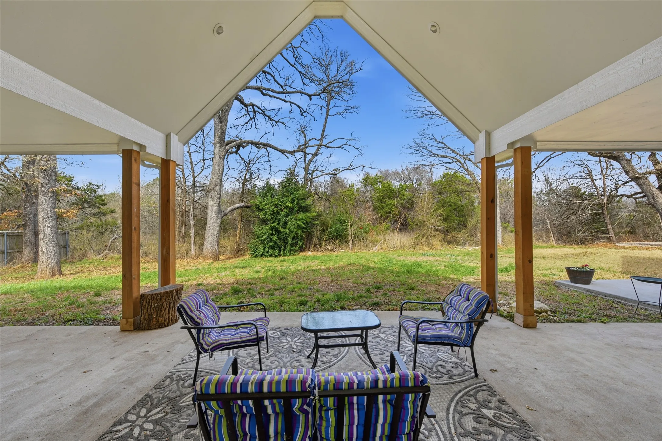 Expansive covered patio featuring a vaulted ceiling, exposed wood posts, and a concrete slab