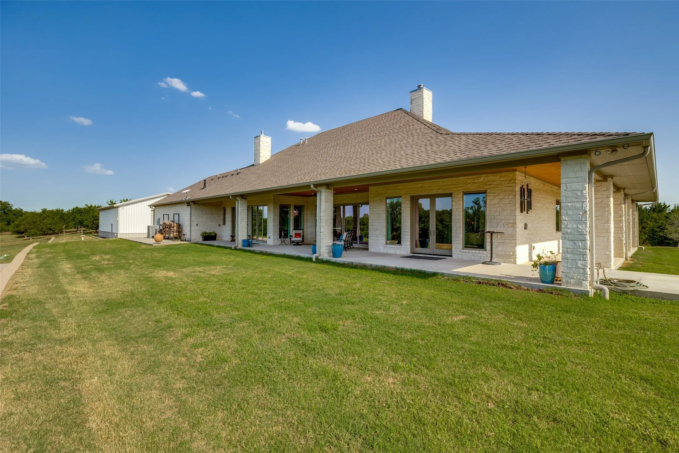 Expansive rear facade featuring a covered patio, multiple glass doors, and a stone exterior
