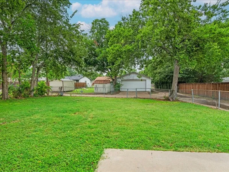 Expansive green lawn with mature trees, a privacy fence, and a detached garage featuring a white overhead door