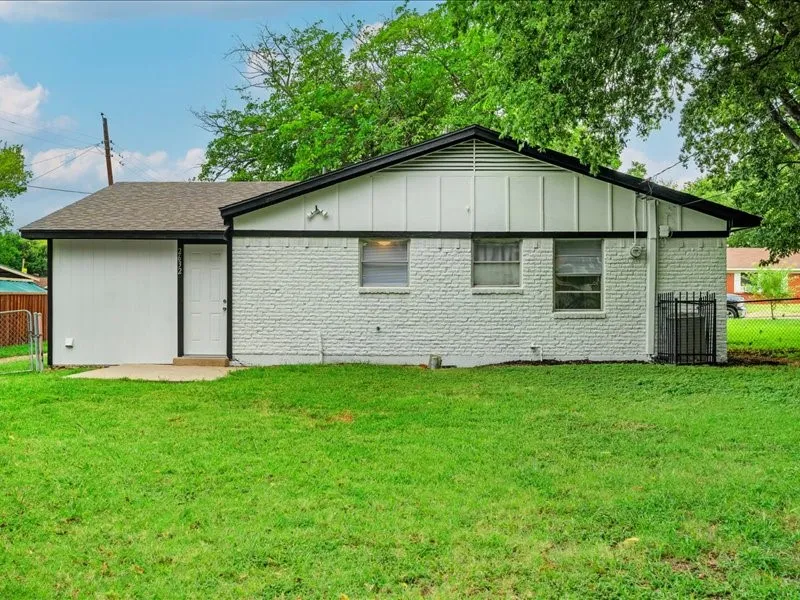 White brick exterior with a dark roof and trim, featuring a concrete patio, a side entry door, and multiple windows
