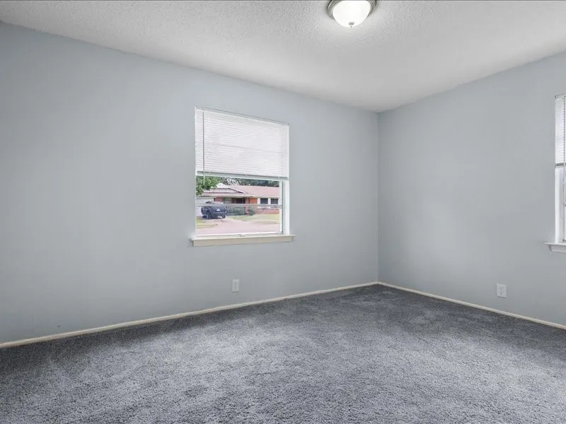 Room featuring light gray wall paint, gray carpeting, a window with horizontal blinds, and a flush-mount ceiling light fixture