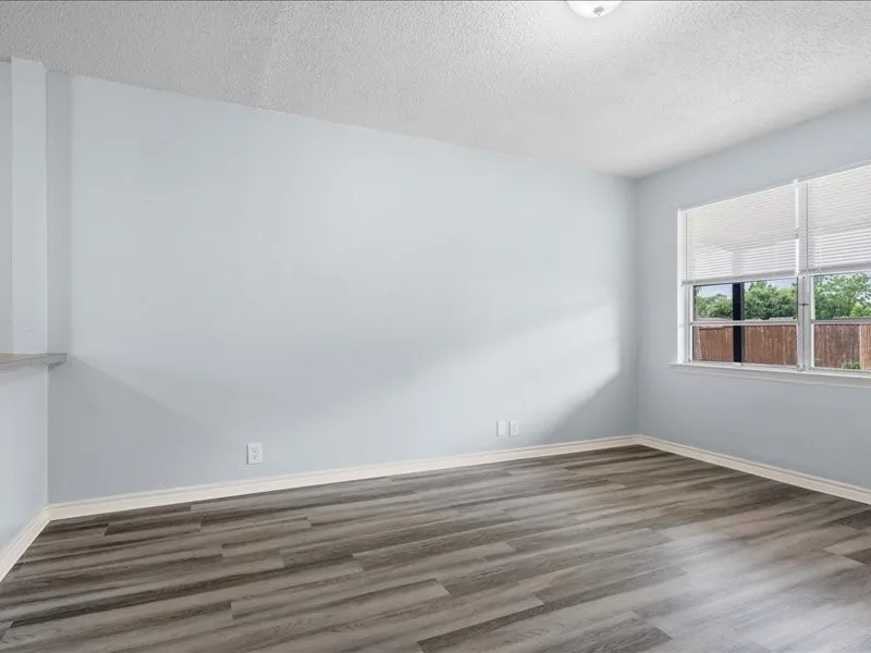 Spacious room featuring wood-finish flooring, light blue walls, and a large window with horizontal blinds