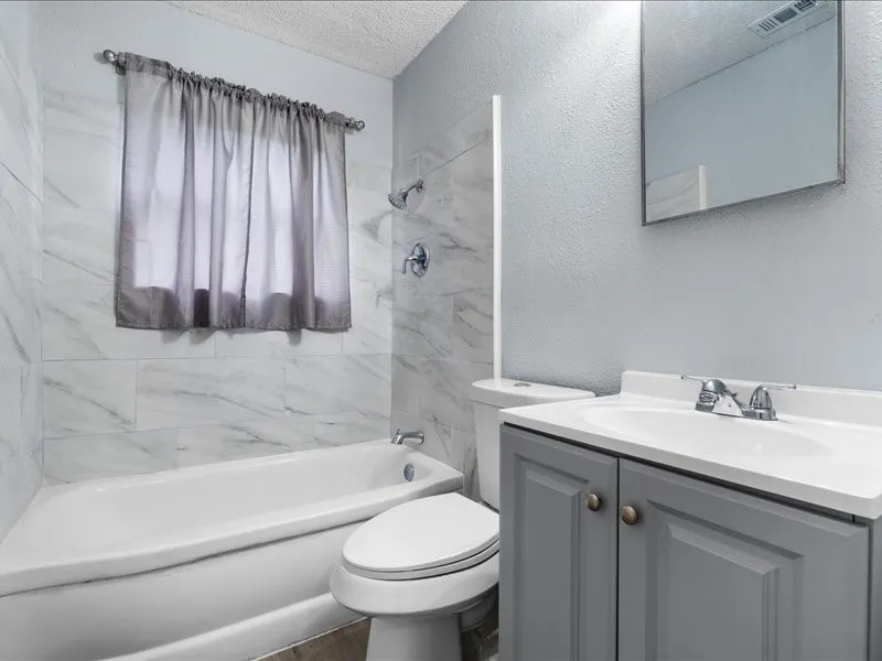 Bathroom featuring a white bathtub, toilet, and a vanity with a white countertop and gray cabinetry
