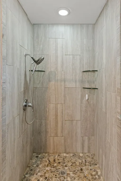 Walk-in shower featuring pebble stone flooring, large format wall tiling, a handheld shower fixture, and recessed lighting