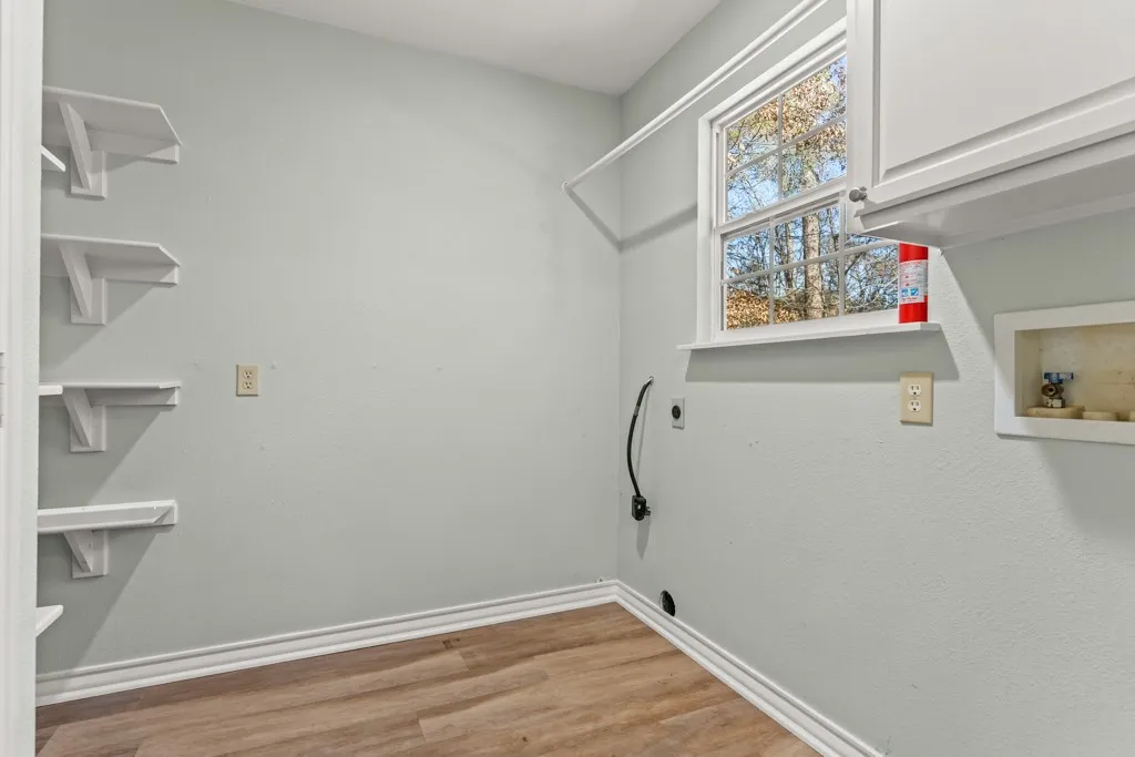Utility room featuring wood-finish flooring, a white window frame, and built-in white cabinetry