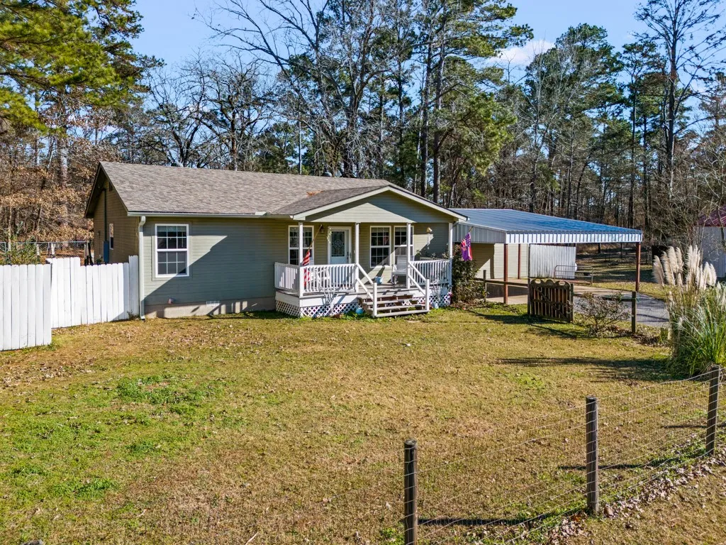 Ranch-style residence featuring a covered front porch with white railings, a gravel driveway, and a detached carport