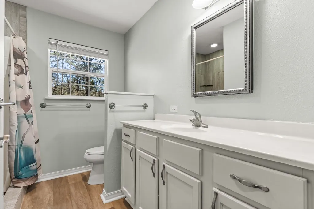Bathroom featuring a single window, white vanity with integrated sink, chrome hardware, wood-finish flooring, and light-colored wall paint