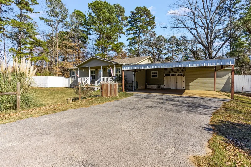 Ranch-style residence featuring a covered front porch, carport, detached garage, and a white privacy fence