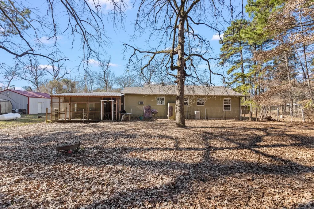 Expansive backyard featuring a screened porch, a detached storage building with a red roof, perimeter fencing, and mature trees