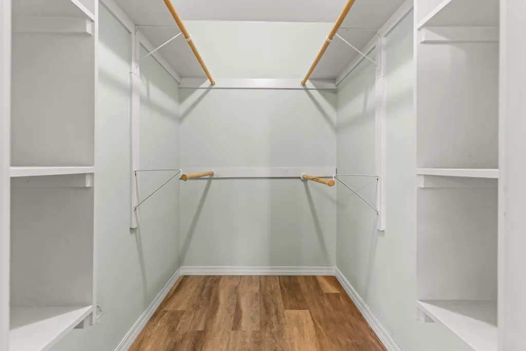 Walk-in closet featuring wood-finish flooring, light-toned wall paint, white trim, custom shelving, and double clothing rods