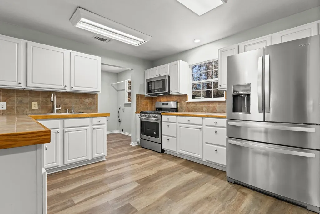 Kitchen featuring white cabinetry, wood-finish countertops, stainless steel appliances, and wood-finish flooring