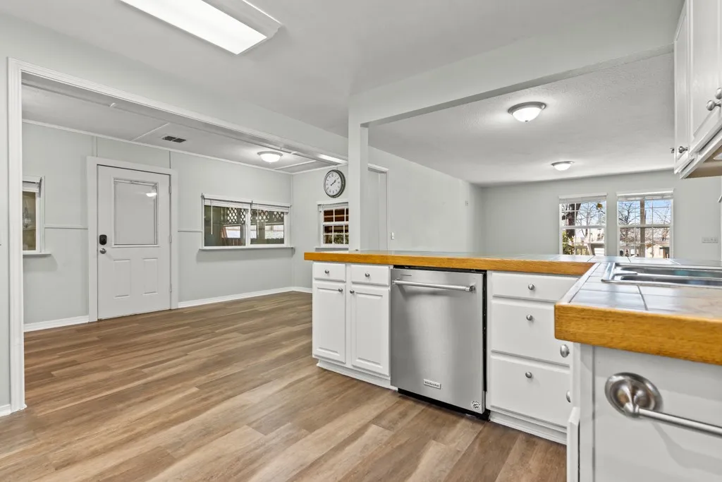 Kitchen featuring wood-finish countertops, white cabinetry with silver hardware, and a stainless steel dishwasher