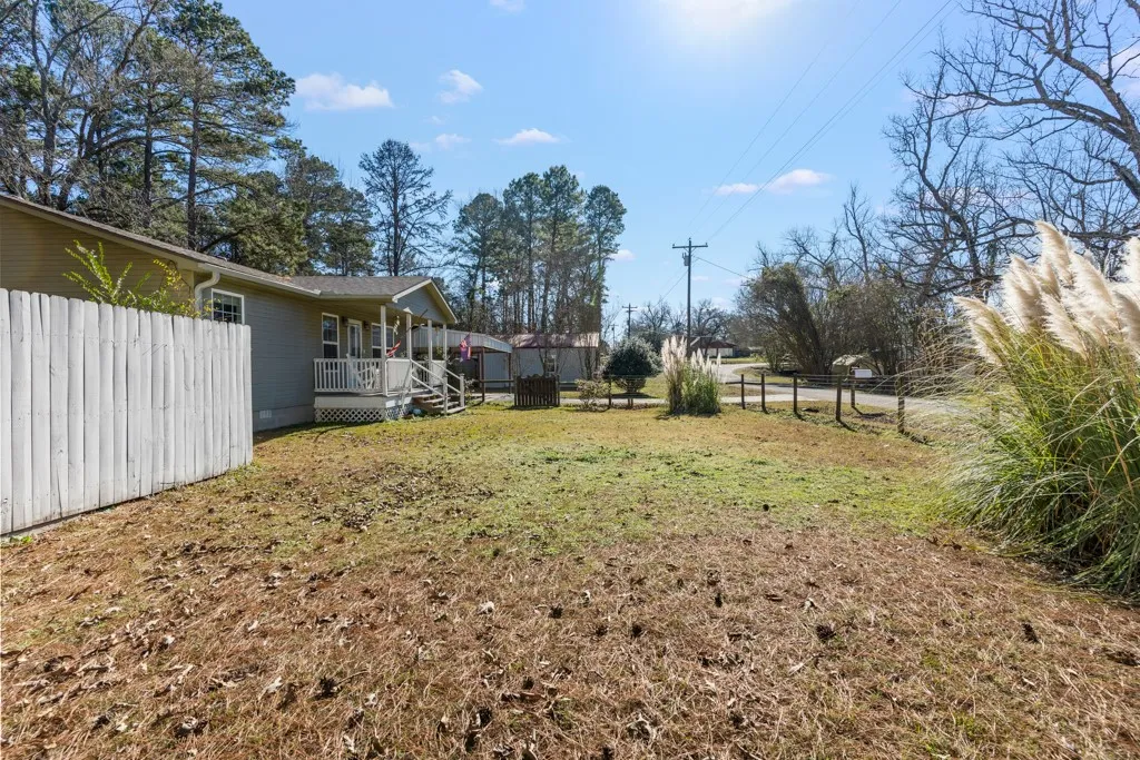 Expansive outdoor space featuring a partial privacy fence, established shrubbery, and a partial wire fence