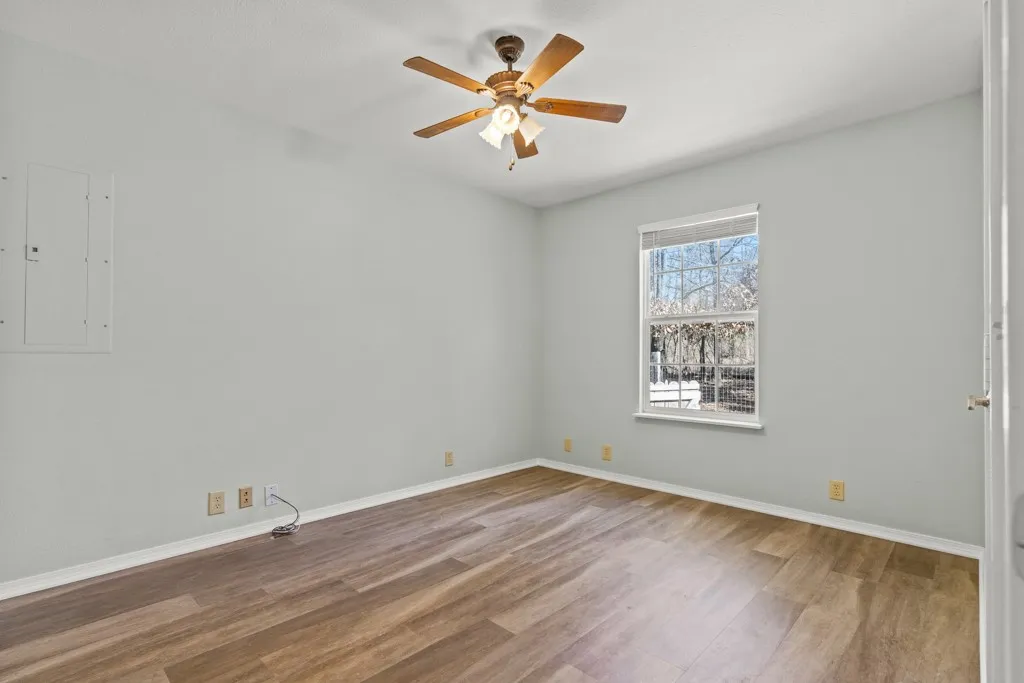 Room featuring wood-finish flooring, light gray walls, a ceiling fan with light fixture, and a window with blinds