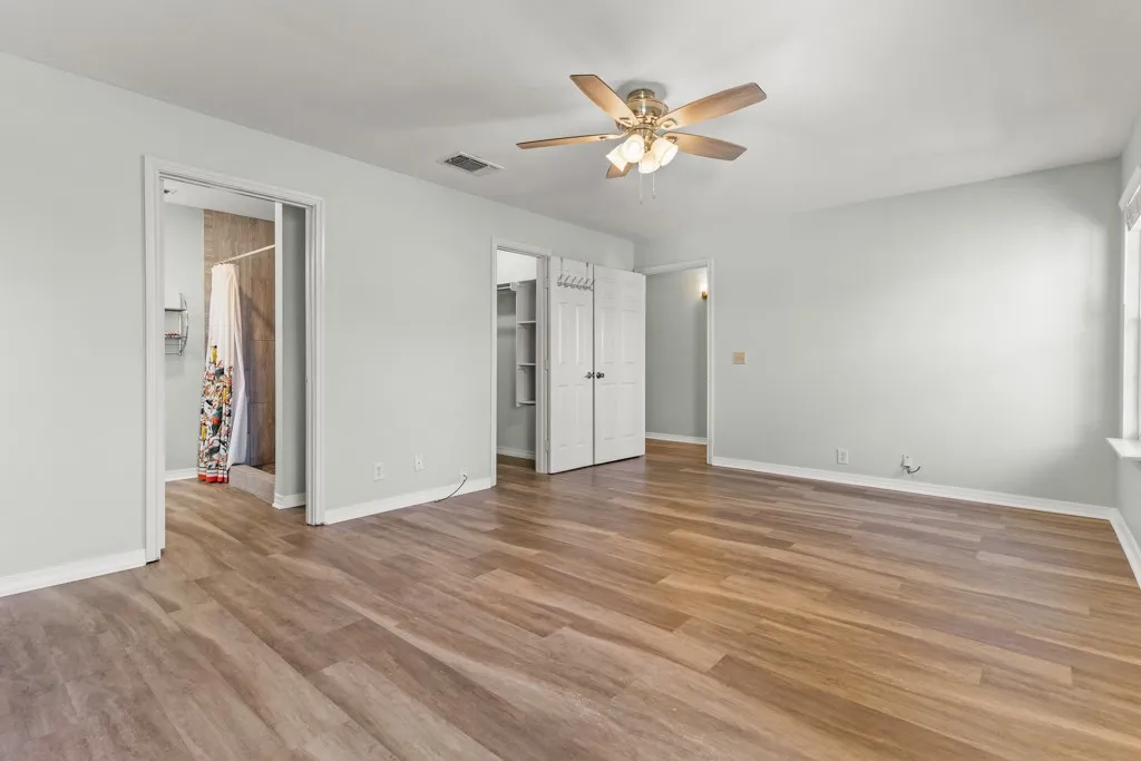 Spacious room featuring wood-finish flooring, a ceiling fan with integrated lighting, bi-fold closet doors, and light gray wall paint