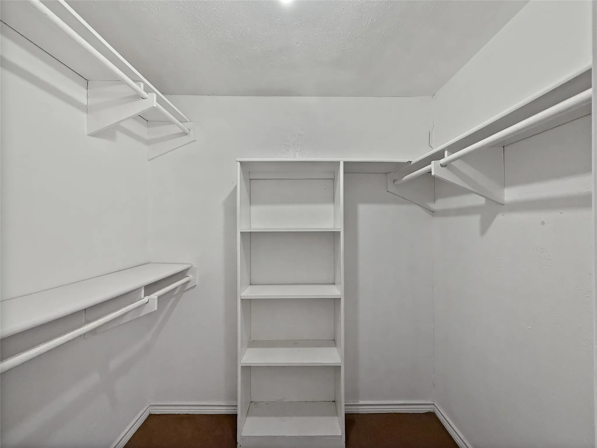 Walk-in closet featuring built-in shelving, two levels of hanging rods, and perimeter baseboards