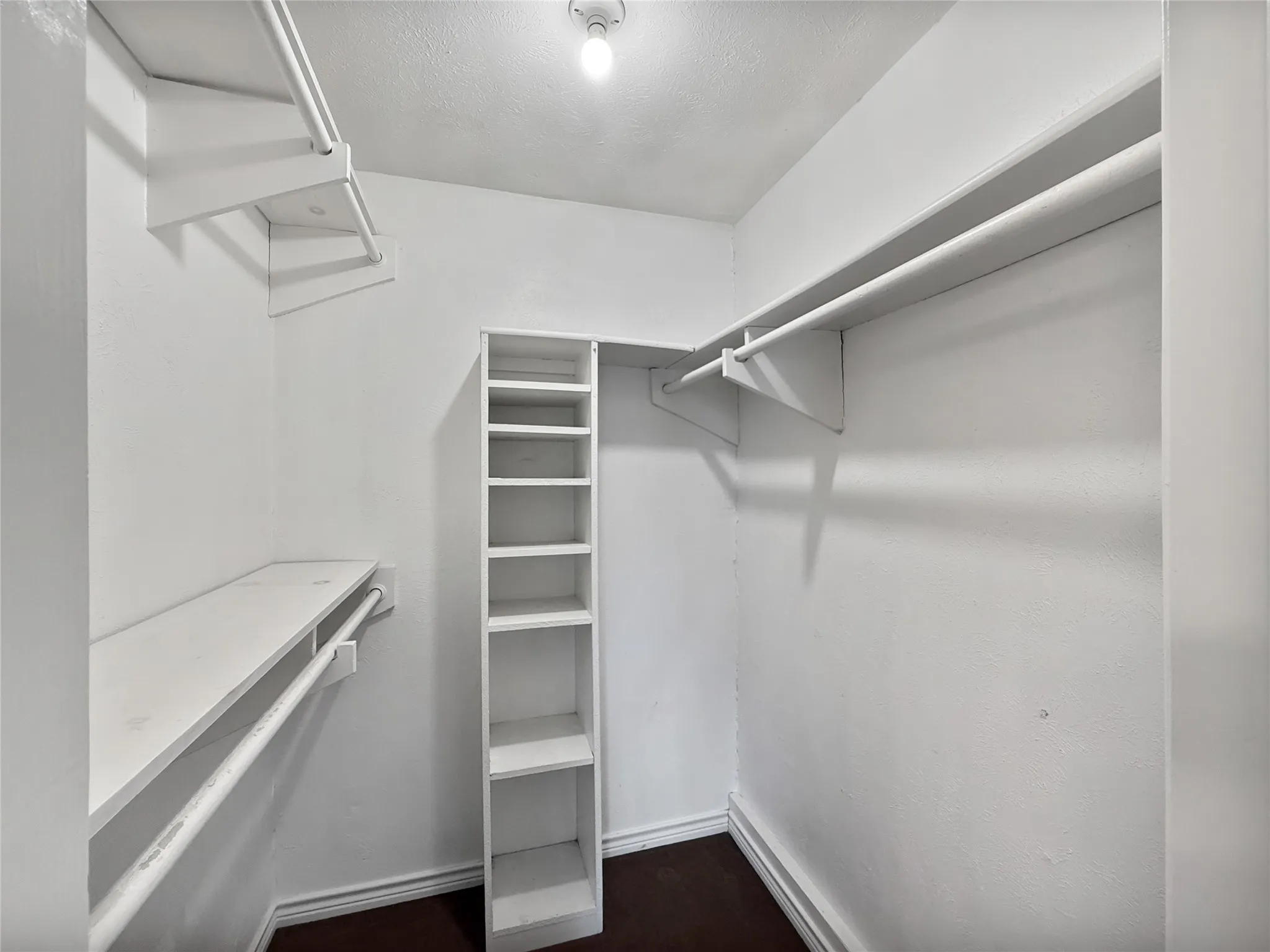 White-painted walk-in closet featuring multiple hanging rods, overhead shelving, and a built-in vertical shelving unit