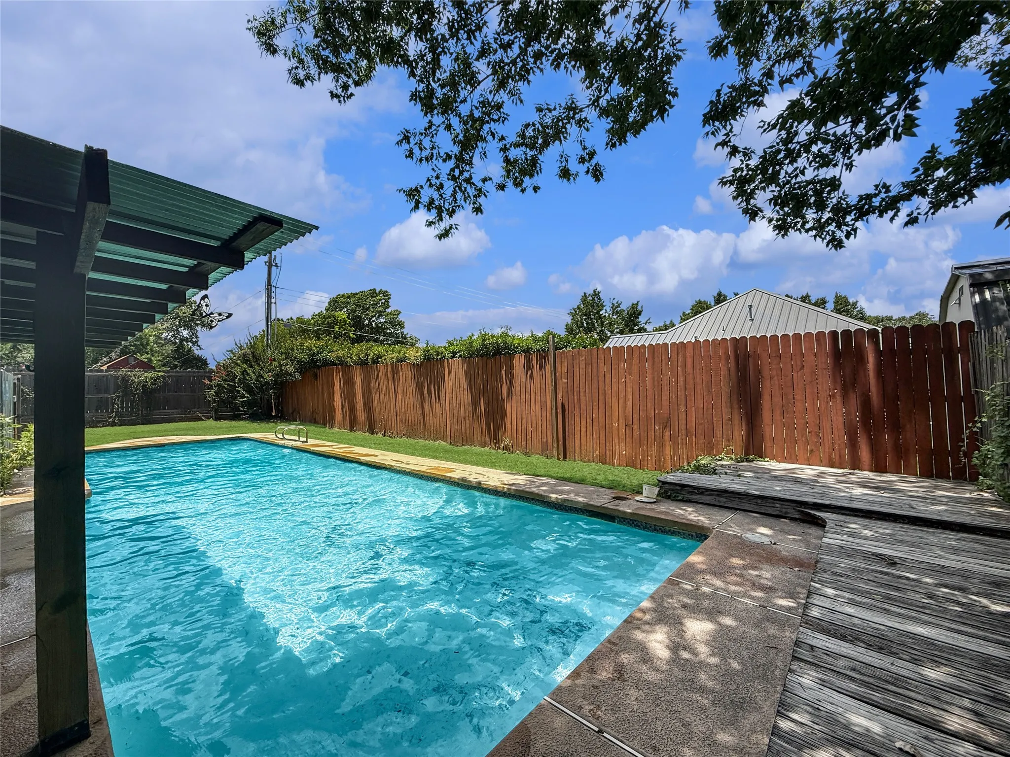 Swimming pool with concrete coping, surrounded by a wood privacy fence and a small grassy area