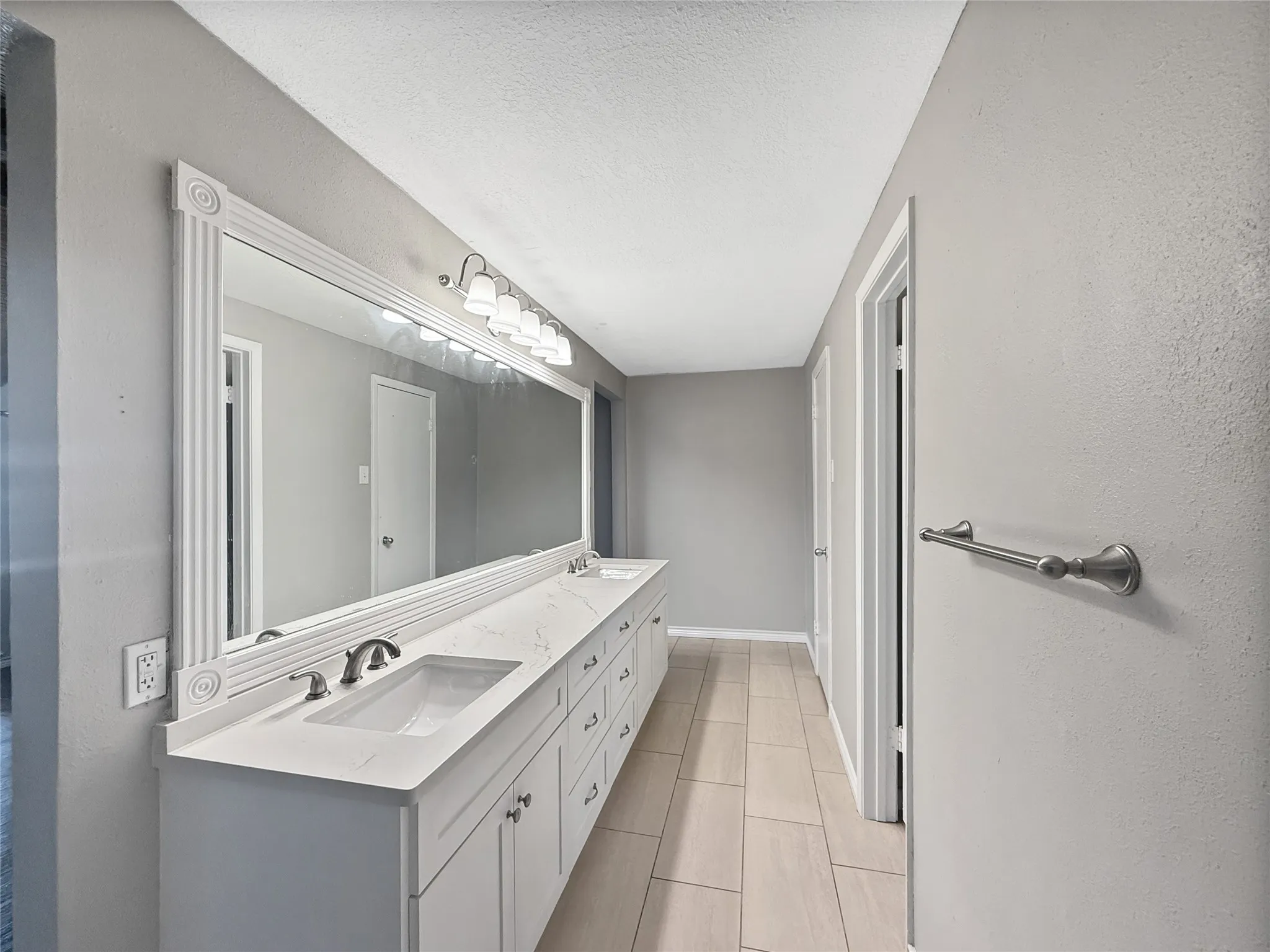 Double vanity featuring white cabinetry, integrated sinks, and a stone-finish countertop, complemented by a large framed mirror with overhead lighting