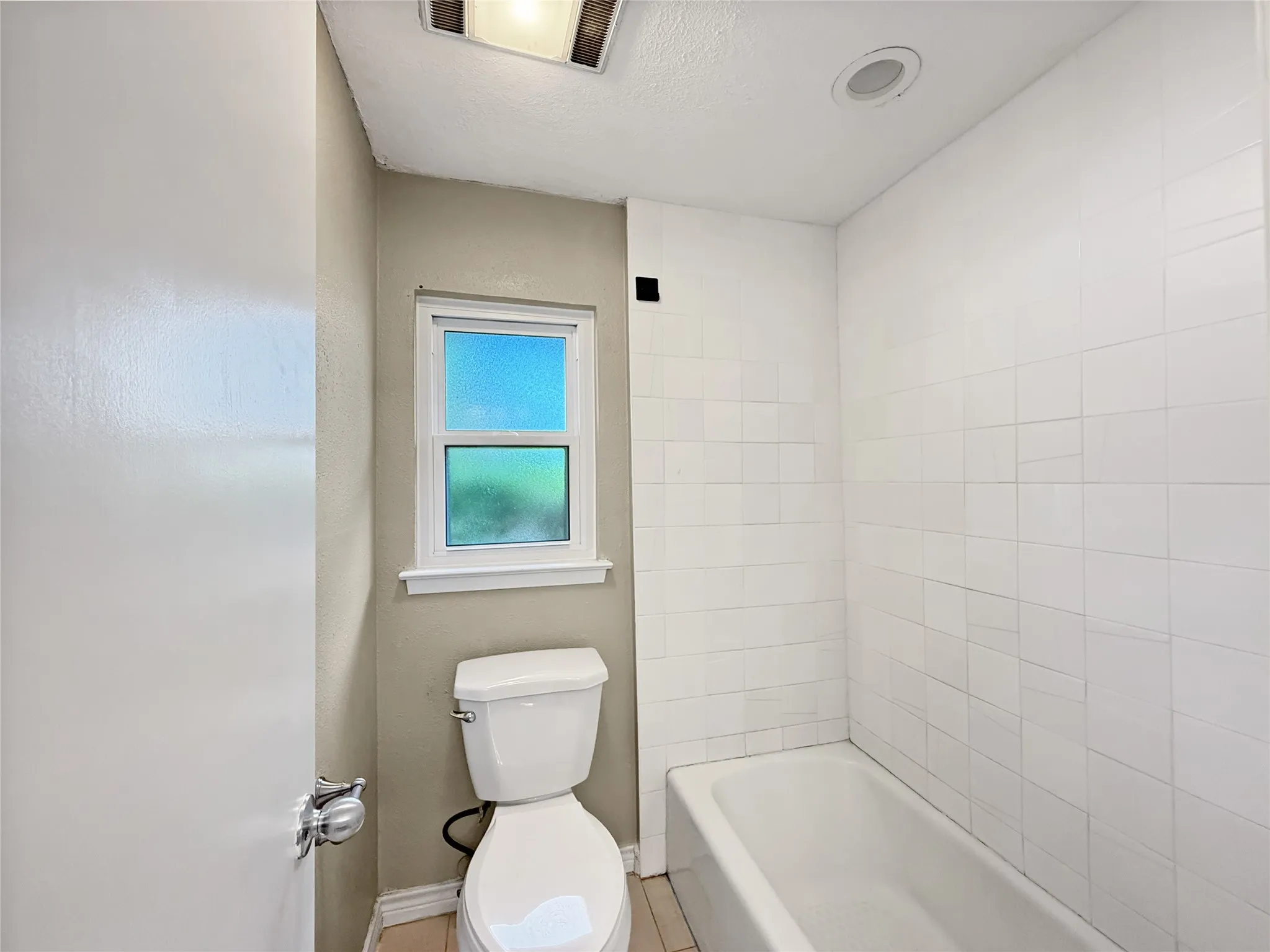 Bathroom featuring a white bathtub, white subway tile surround, and a white toilet