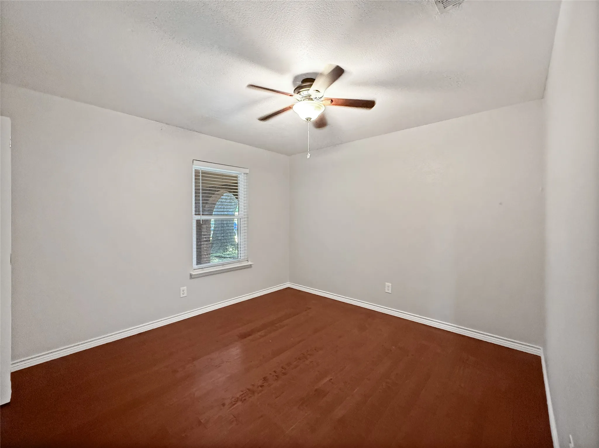 Room featuring wood-finish flooring, light-toned walls, and a ceiling fan with integrated lighting