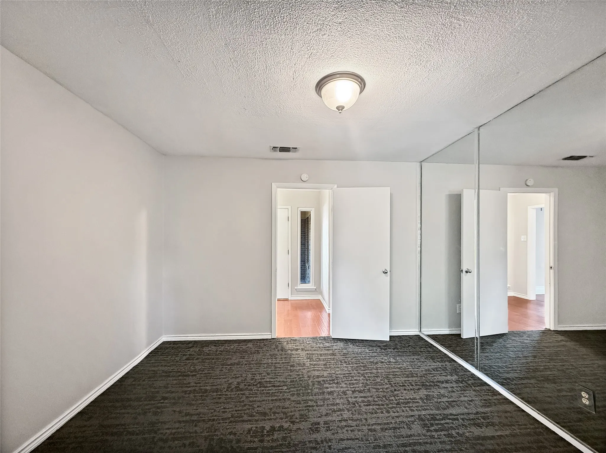 Interior room featuring textured carpet flooring and a full mirrored wall