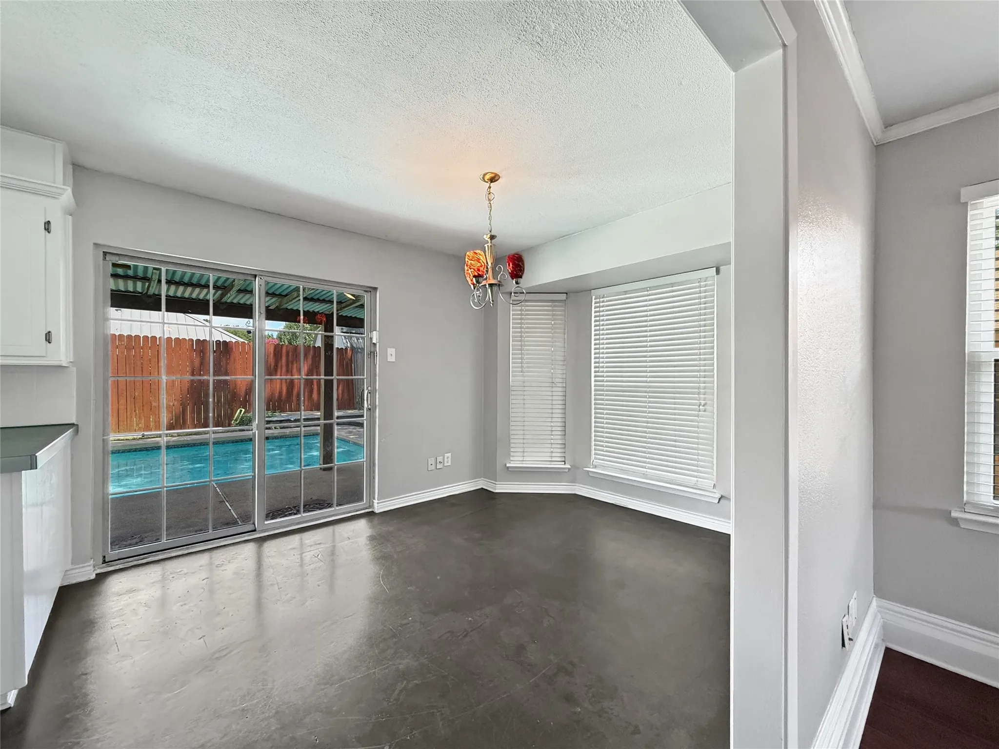Dining space featuring sliding glass doors overlooking a swimming pool, dark concrete flooring, and a bay window with blinds