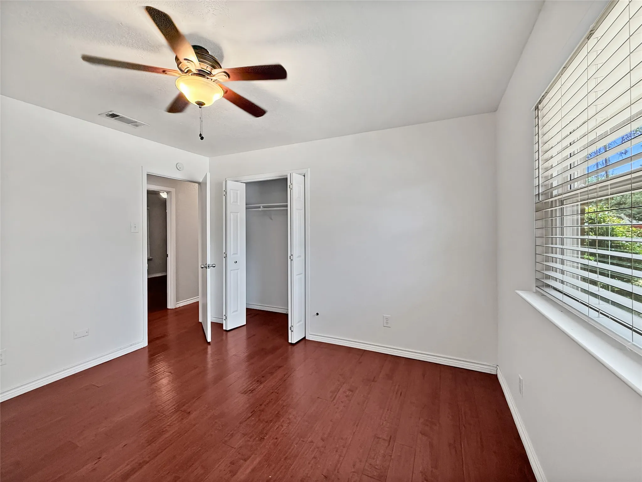 Room featuring wood-finish flooring, a ceiling fan with integrated lighting, window blinds, and a built-in closet with bifold doors