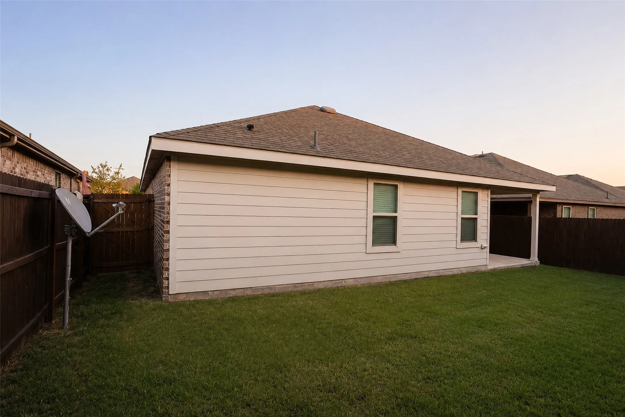 Expansive backyard featuring a manicured lawn, full perimeter fencing, and a covered concrete patio