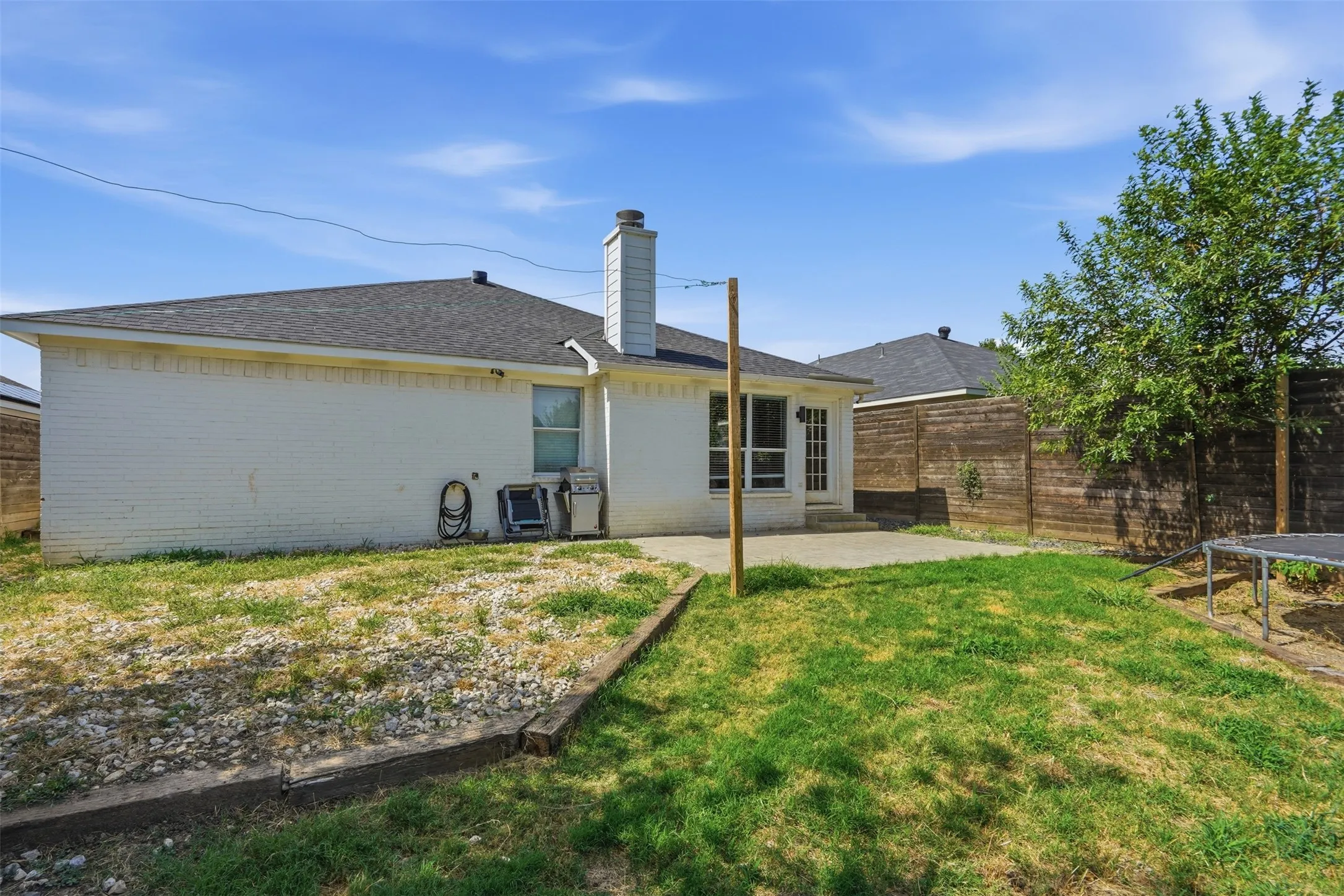 Expansive backyard featuring a concrete patio, white brick exterior, dark shingle roof, and a mature tree