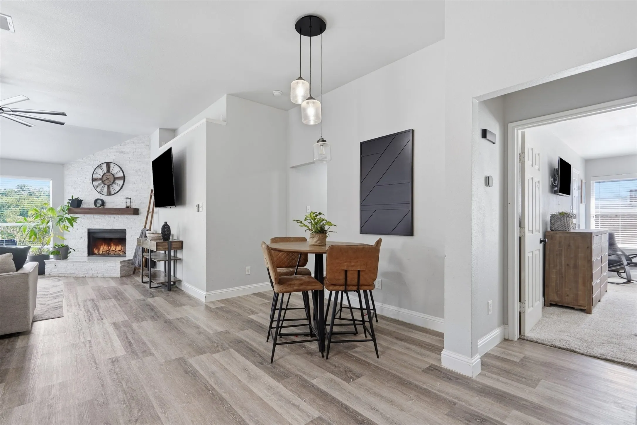 Open-concept living space featuring wood-finish flooring, a white brick fireplace with a wood mantle, and a vaulted ceiling