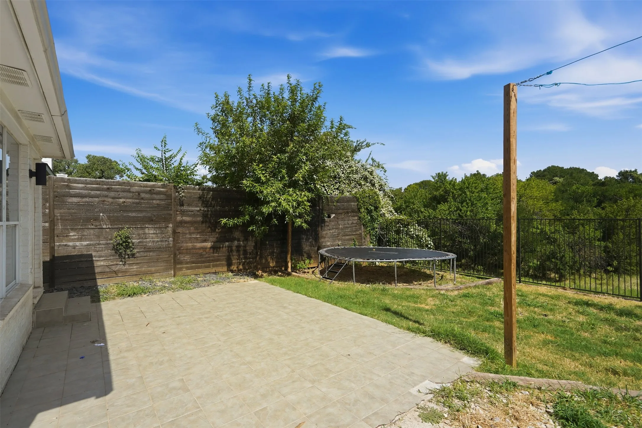 Expansive outdoor patio area featuring textured pavers, an adjacent grassy yard, and mature perimeter trees