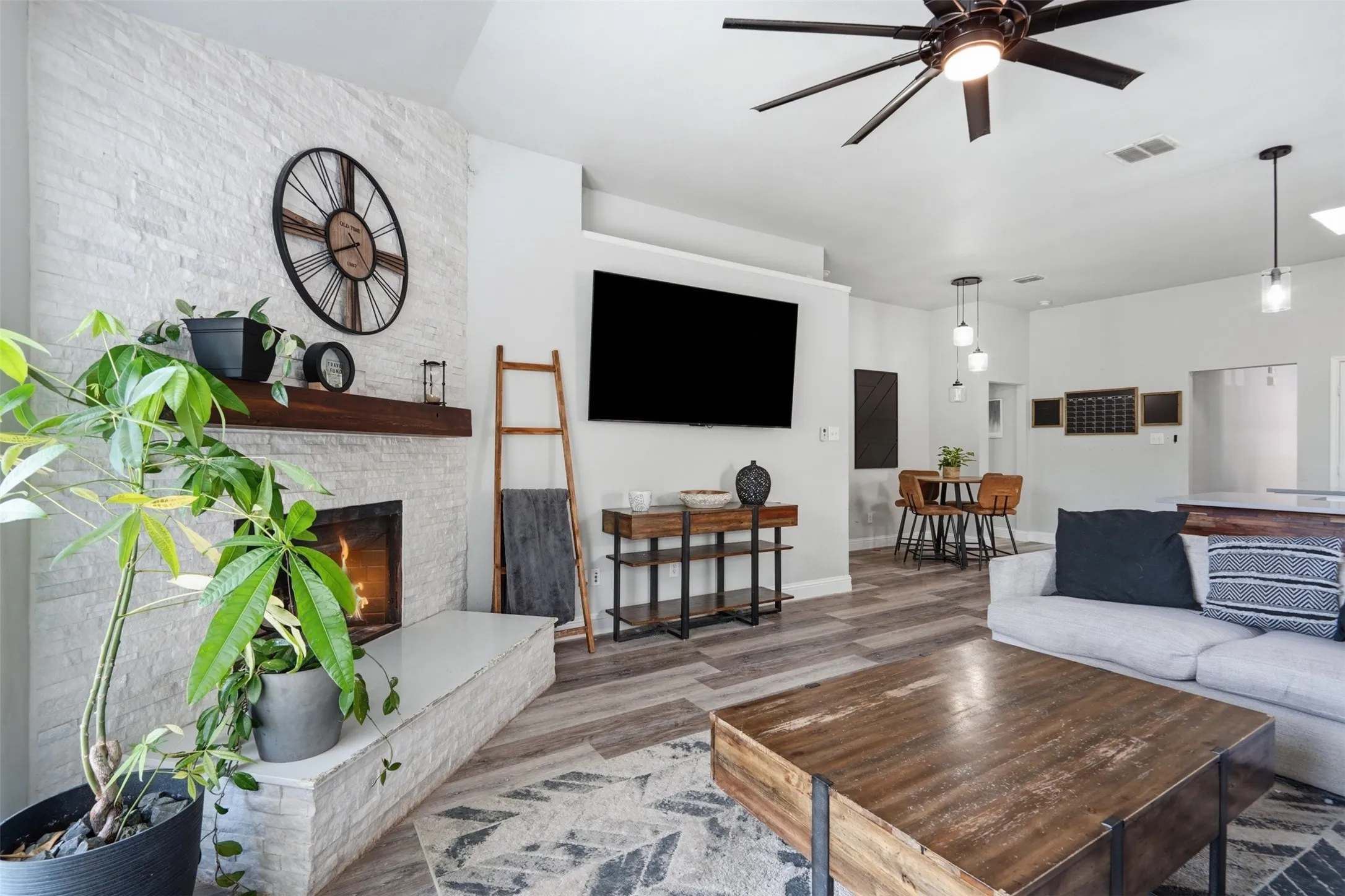 Living area featuring a floor-to-ceiling white stacked stone fireplace with a wood mantel, wood-finish flooring, and a modern ceiling fan